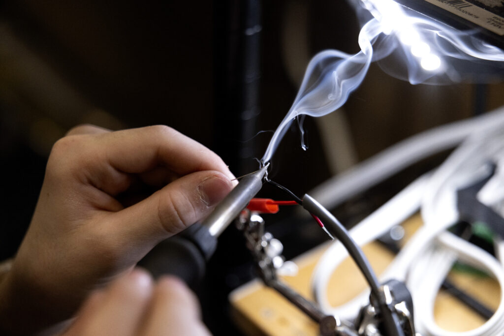 Hands are featured soldering wires together. Smoke wafts upward.