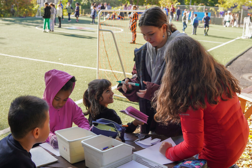 A senior student mentors junior students at recess on the football field.