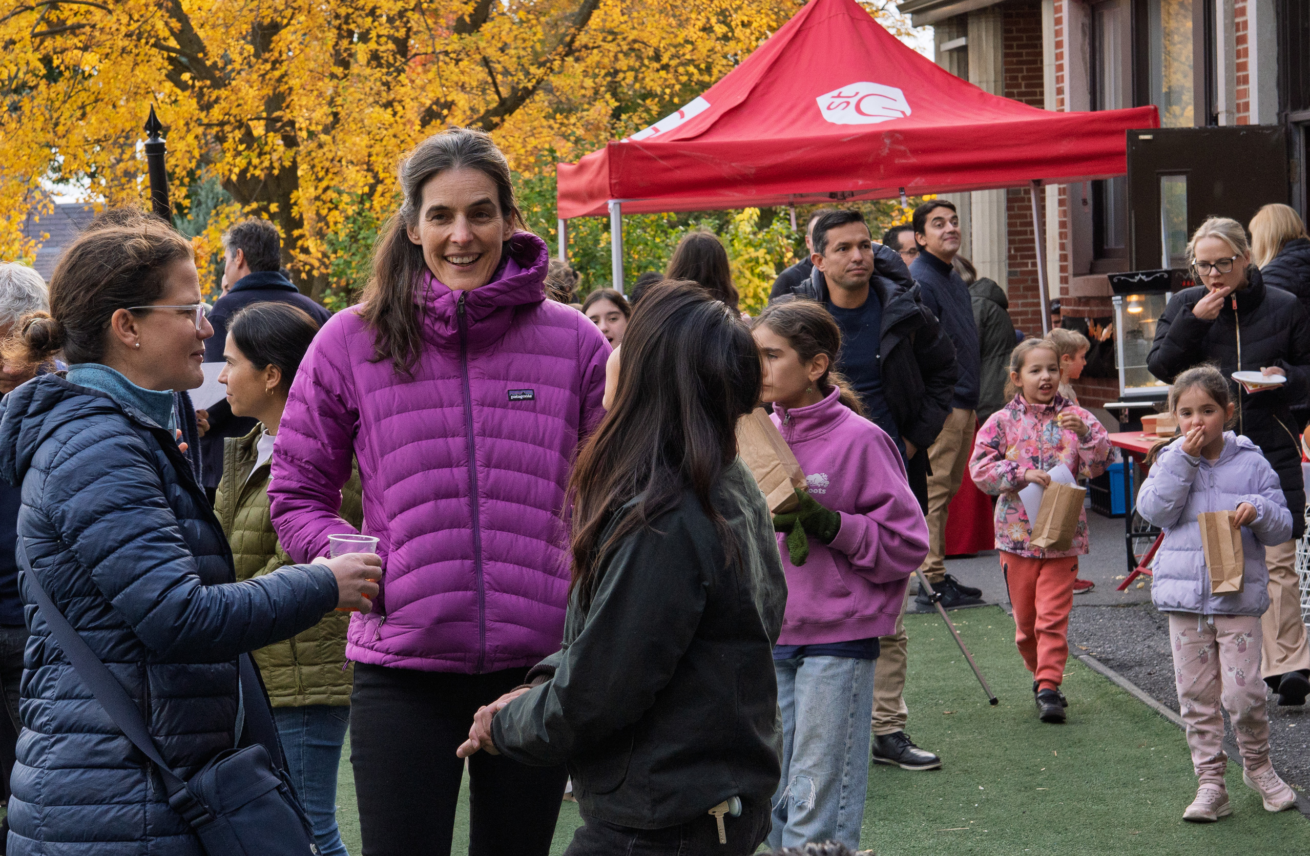 Community members and children gather outside at fall fest. A red tent is in the background.