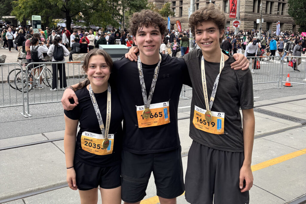 Three Grade 11 students stand facing the camera. Marathon medals are around their nexks. 