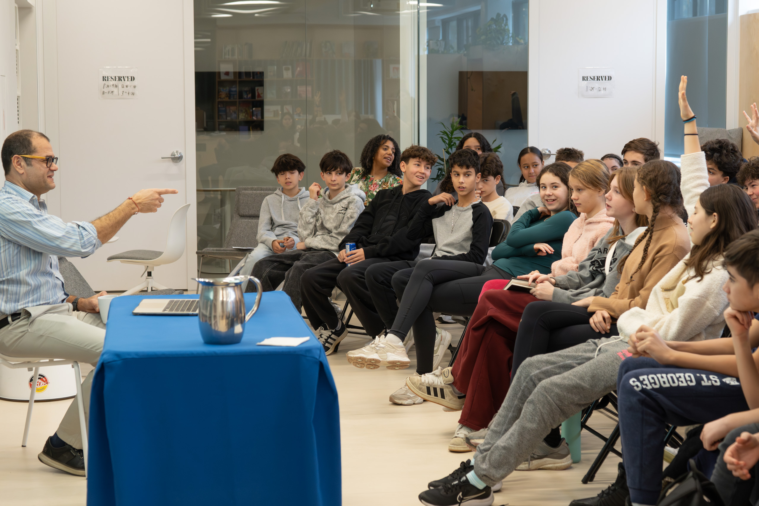 A man points at a group of high school students sitting down in a room. He is behind a table.
