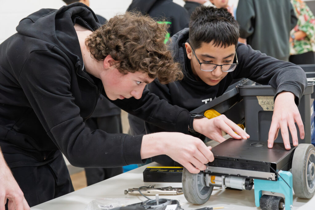 Two male students work on the chassis of their robot.