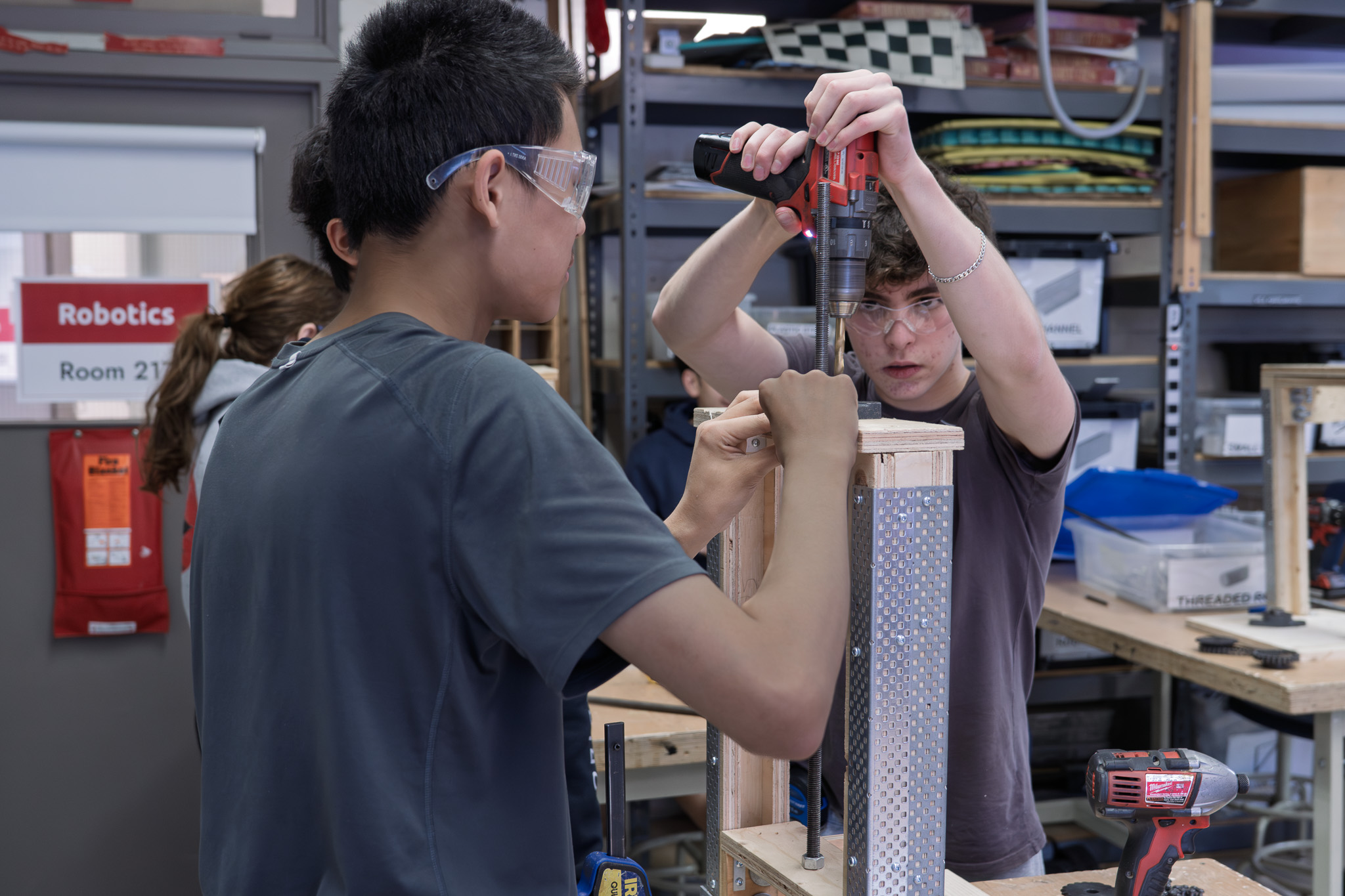 Student uses a Milwaukee drill while another student assists in the robotics lab.