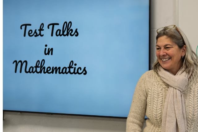 A woman stands in front of a white board that says test talks.