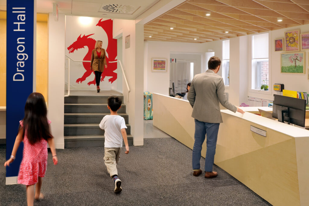 Two students and a man walk through a school reception area. There is dragon signage on the wall.