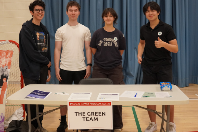 4 students stand behind a table in a gymnasium.