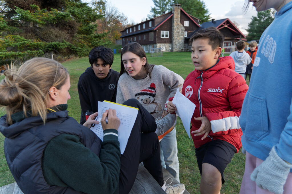Students discuss something with a teacher outdoors.