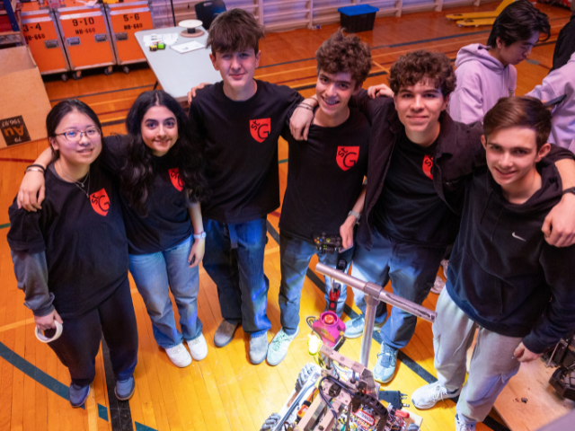 A group of students stand together wearing robotics t-shirts.