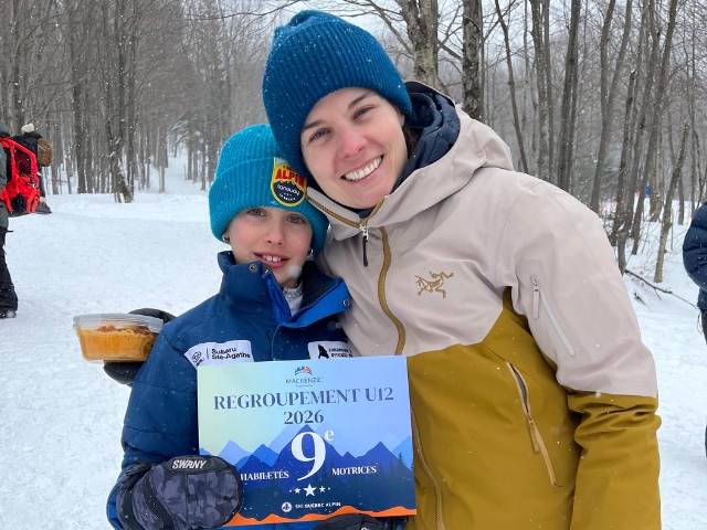 A girl skier and her mother stand at the bottom of a skihill.