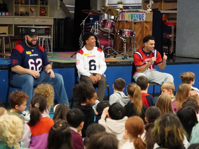Three sports players speak in front of a crowd of students