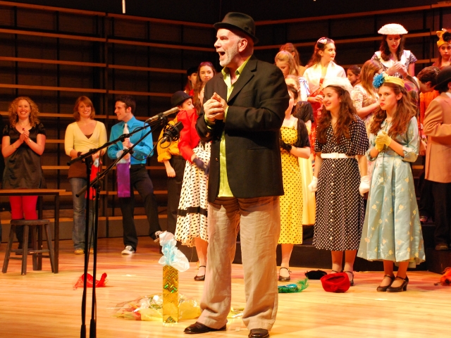 A man speaks onstage in a hat.