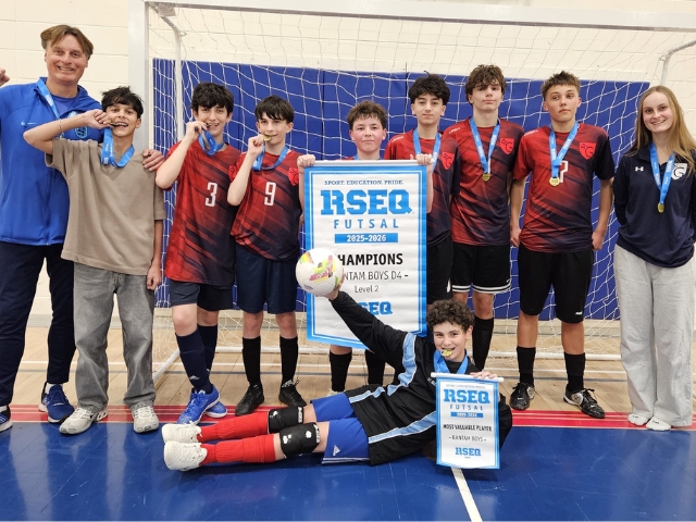 Teenage boy soccer players hold a championship banner in a high school gym.