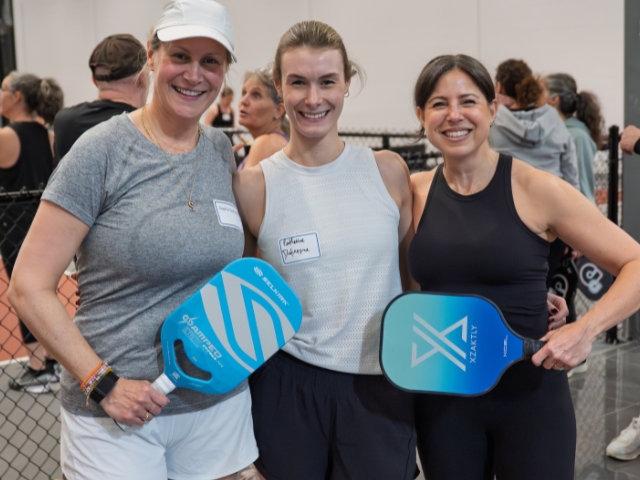 Three women hold pickleball rackets.