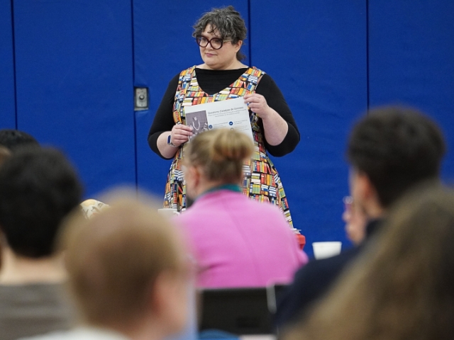 A woman stands before colleagues.