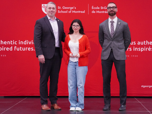 A female High School student receives an award against a red background. She is flanked by two men in suits.