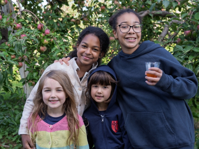 A group of 4 girls stand in an apple orchard ranging from 6 to 12 years old